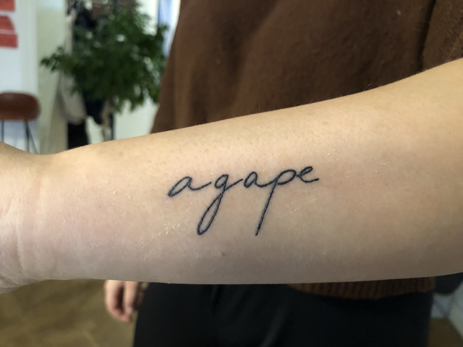 Unterarm mit dem tätowierten Schriftzug agape in feiner Handschrift
