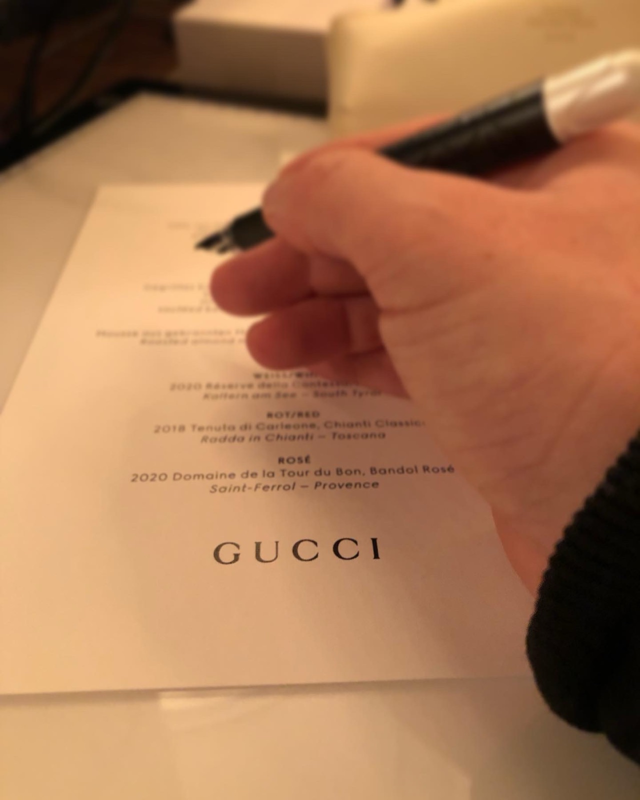Eine Hand vollendet mit dem Stift ein handgeschriebenes Menü auf einer Gucci-Karte